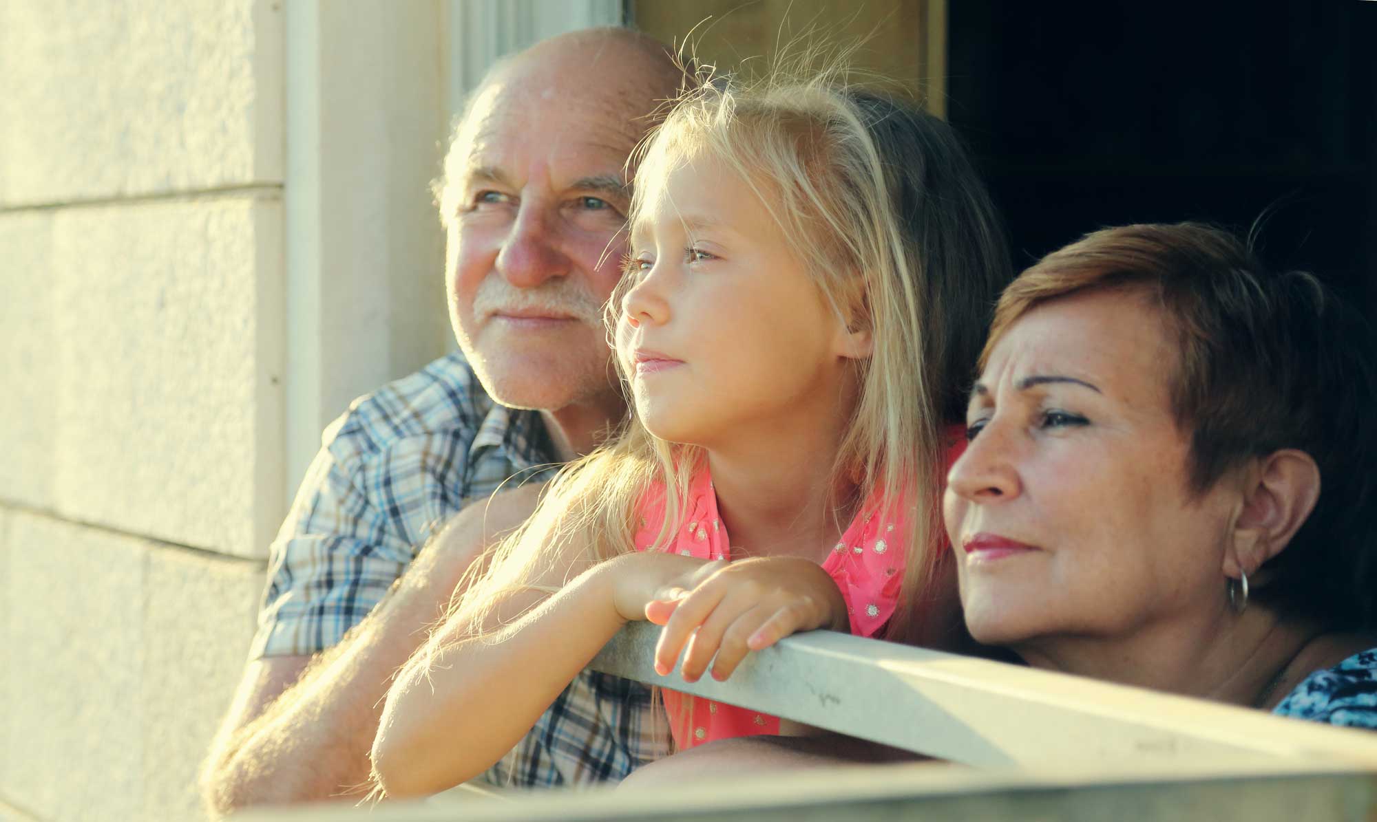 A little girl sitting on the arm of an older man and woman.