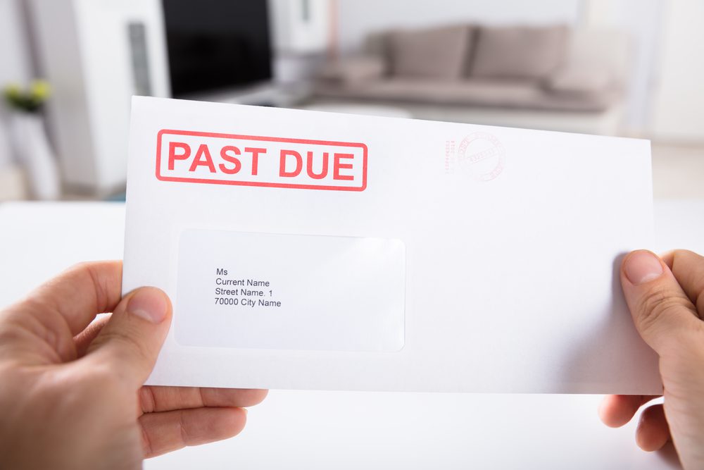 A person holding up an envelope that says past due.