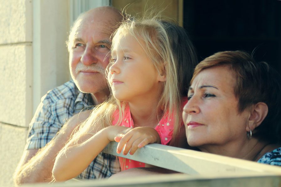 A little girl sitting on the arm of an older man and woman.